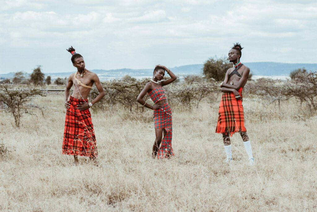 Three people in traditional tribal attire posing in a vast African grassland.